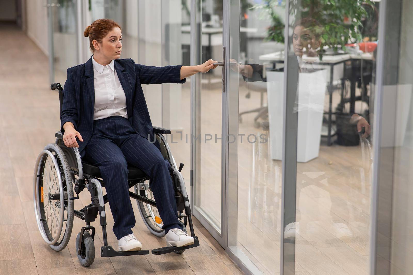 Red-haired caucasian woman in a wheelchair trying to open the door in the office