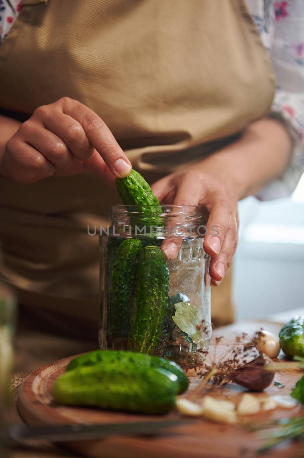 Close-up of a woman, housewife in beige chef's apron, makes pickled cucumbers at home kitchen. Homemade conservation of organic harvested seasonal vegetables. Pickling. Canning. Marinating