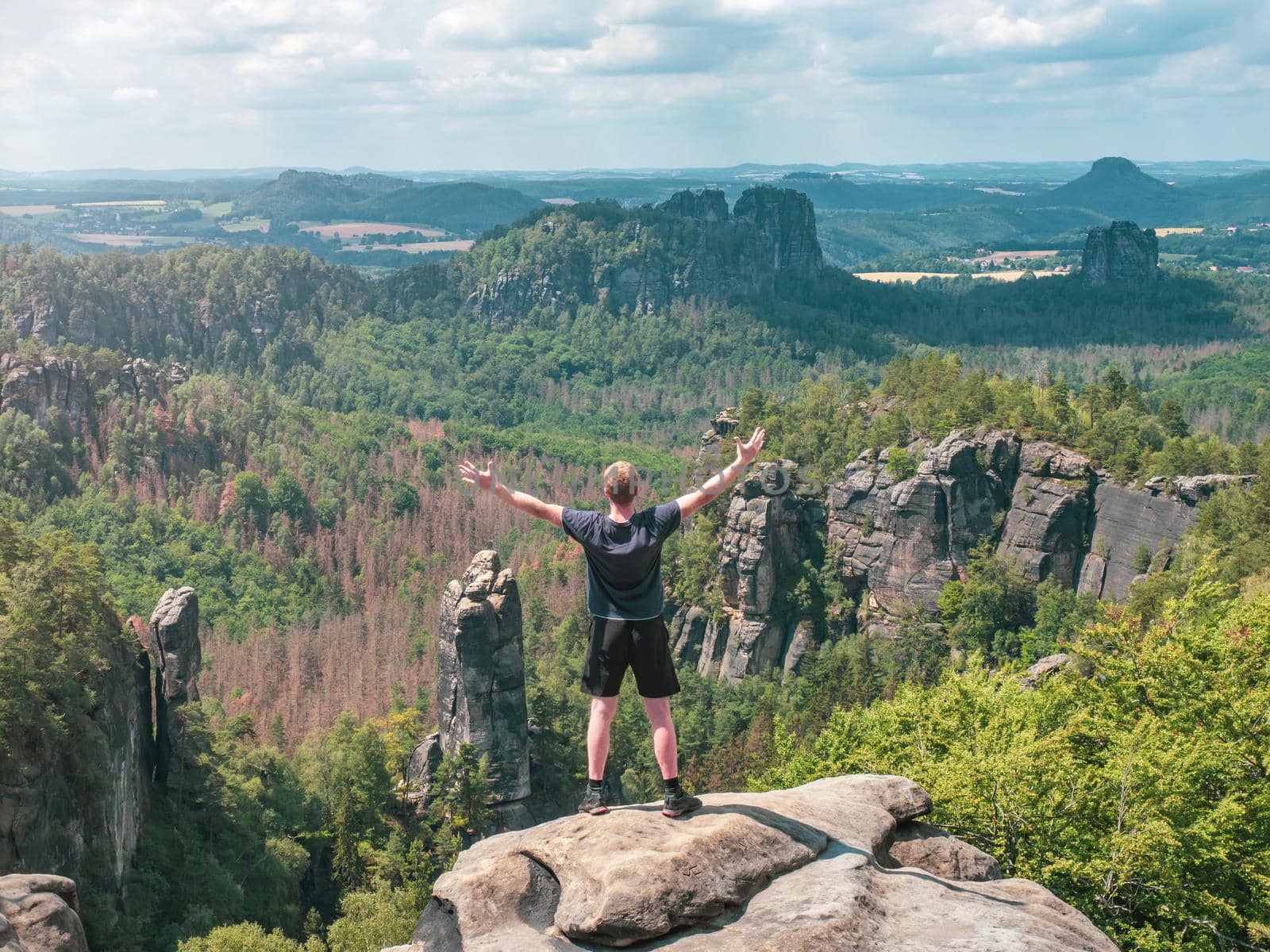 Hiker shouts greetings into valley bellow Carolafelsen rock, Grossen Dom and jagged mountains Schrammsteine and Falkenstein