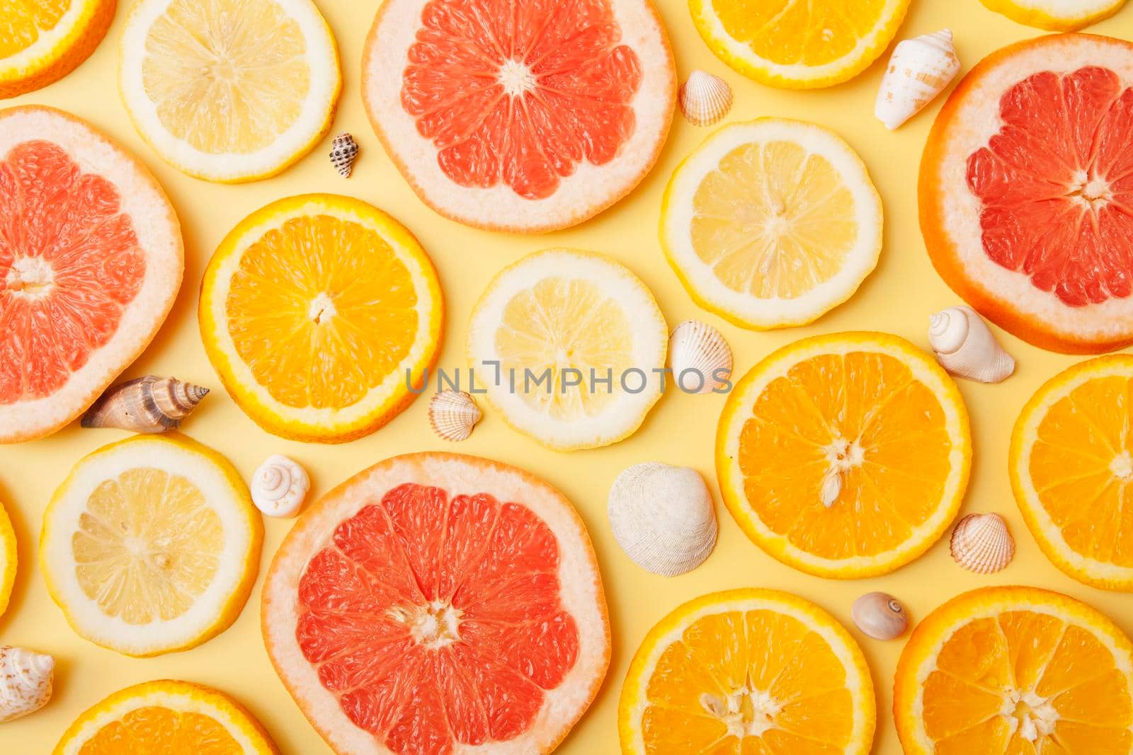 Flat lay slices of orange, grapefruit and lemon with shells on a yellow background. Summer citrus pattern by ssvimaliss