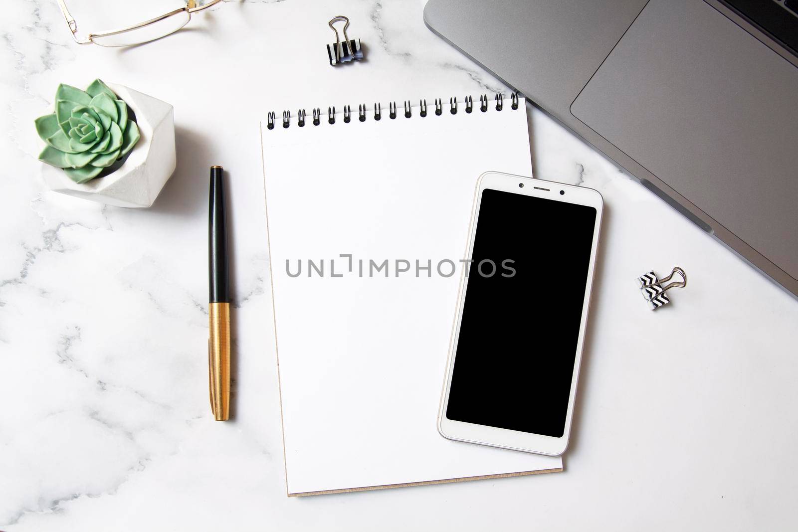 Top view workspace with a notebook mock-up, smartphone, laptop on a marble background. Desktop business concept