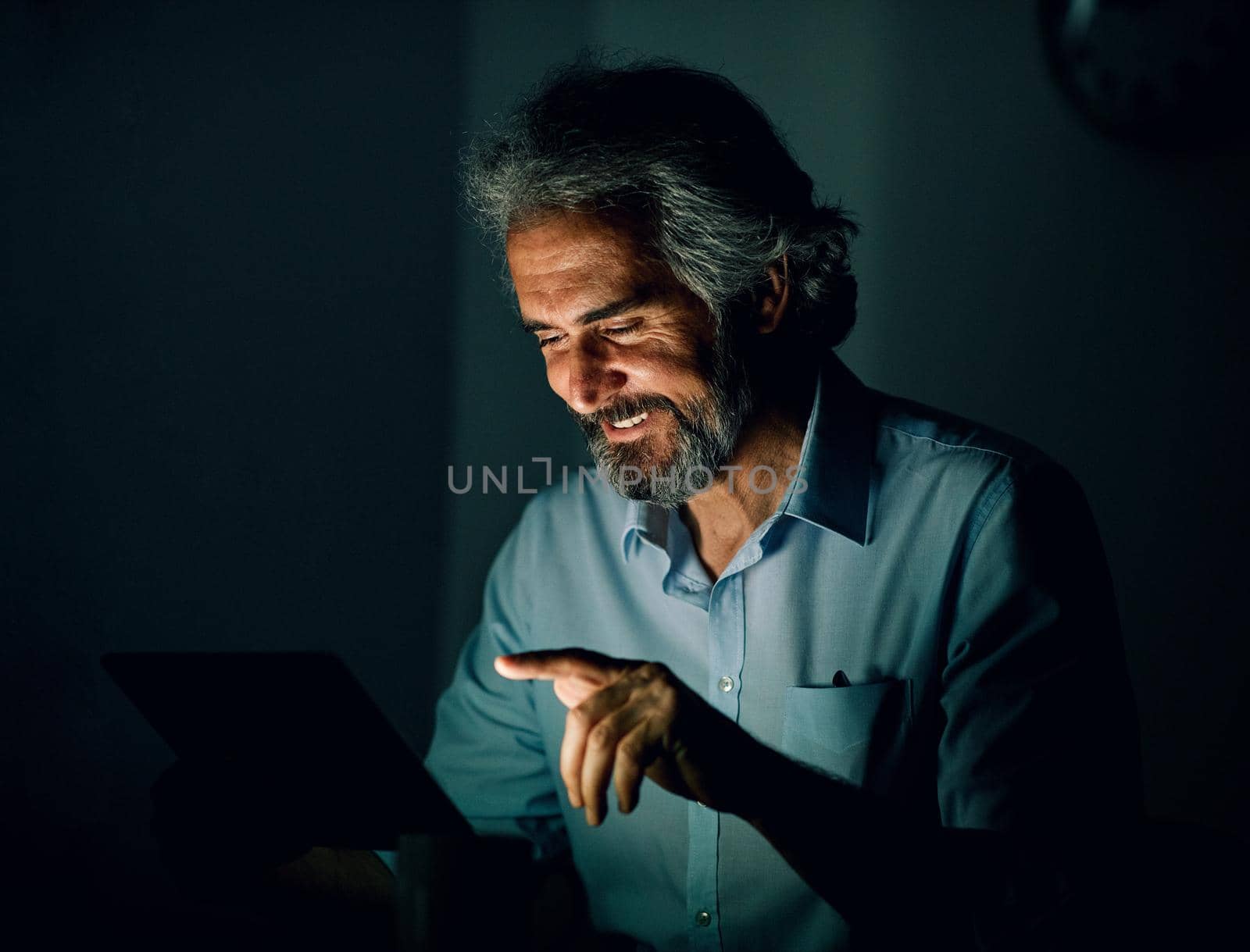 Portrait of a senior businessman with tablet or laptop working late at night in office