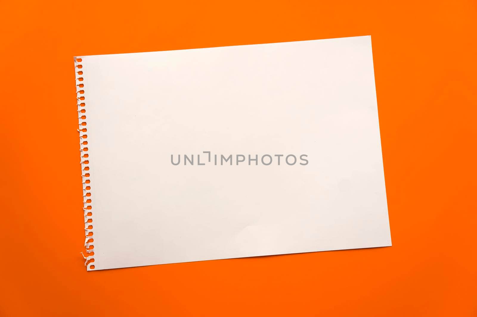 Blank sheet of paper space for design and lettering on a beautiful orange background. A sheet of perforated paper torn from a notepad rests obliquely on the surface. Square sheet of paper copyspace