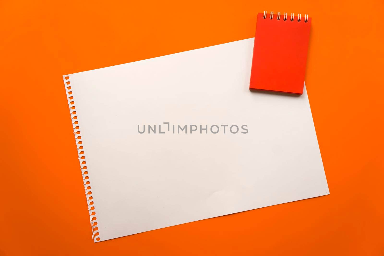 Blank sheet of paper space for design and lettering on a beautiful orange background red notepad sheet. Perforated sheet torn from notepad obliquely lying on the surface. Square sheet of paper copyspace