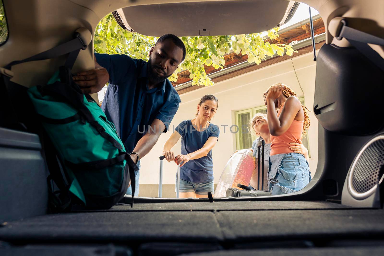 Diverse people loading luggage in trunk, preparing car with trolley and travel bags to leave on holiday trip. Travelling together on vacation adventure during summer, seaside journey.