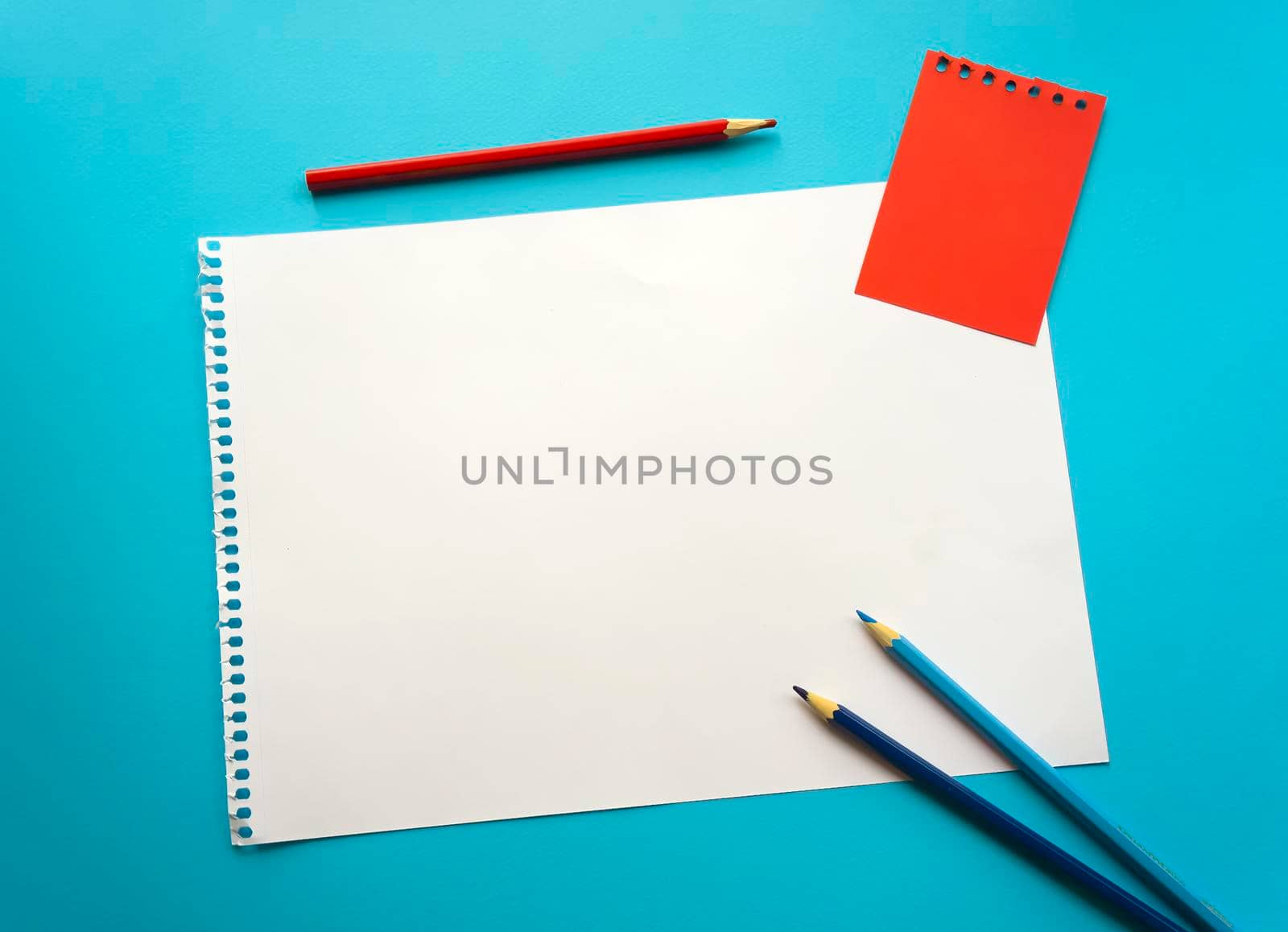 Blank sheet of paper space for design and lettering on a beautiful blue background, blue pencils. A sheet of perforated paper torn from a notepad rests obliquely on the surface. Square sheet copyspace