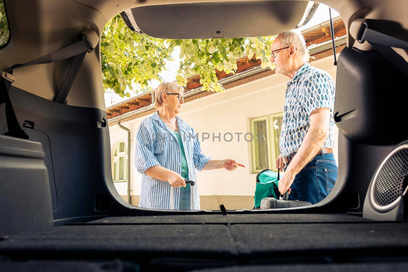 Old couple loading travel bags in trunk to leave on vacation journey with vehicle. People travelling together on retirement holiday trip with trolley and baggage, leisure activity.