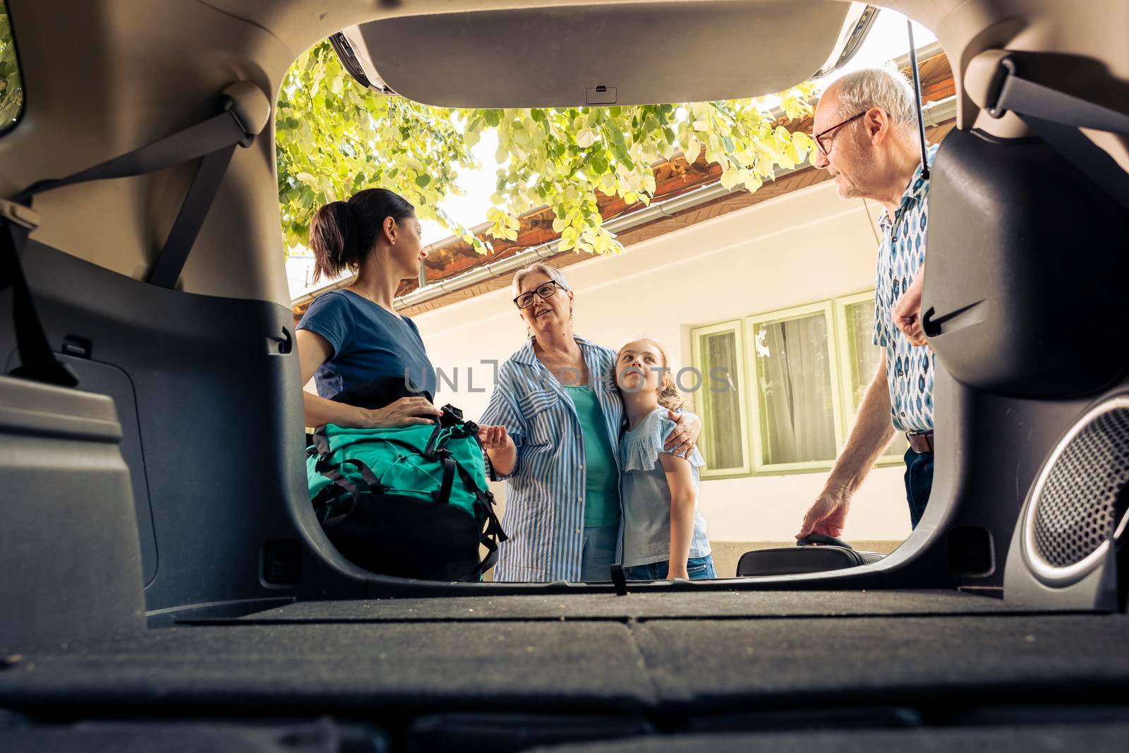 Caucasian family going on seaside holiday with luggage and bags, loading baggage in automobile trunk. Little girl with mother and grandparents travelling on vacation trip with vehicle.
