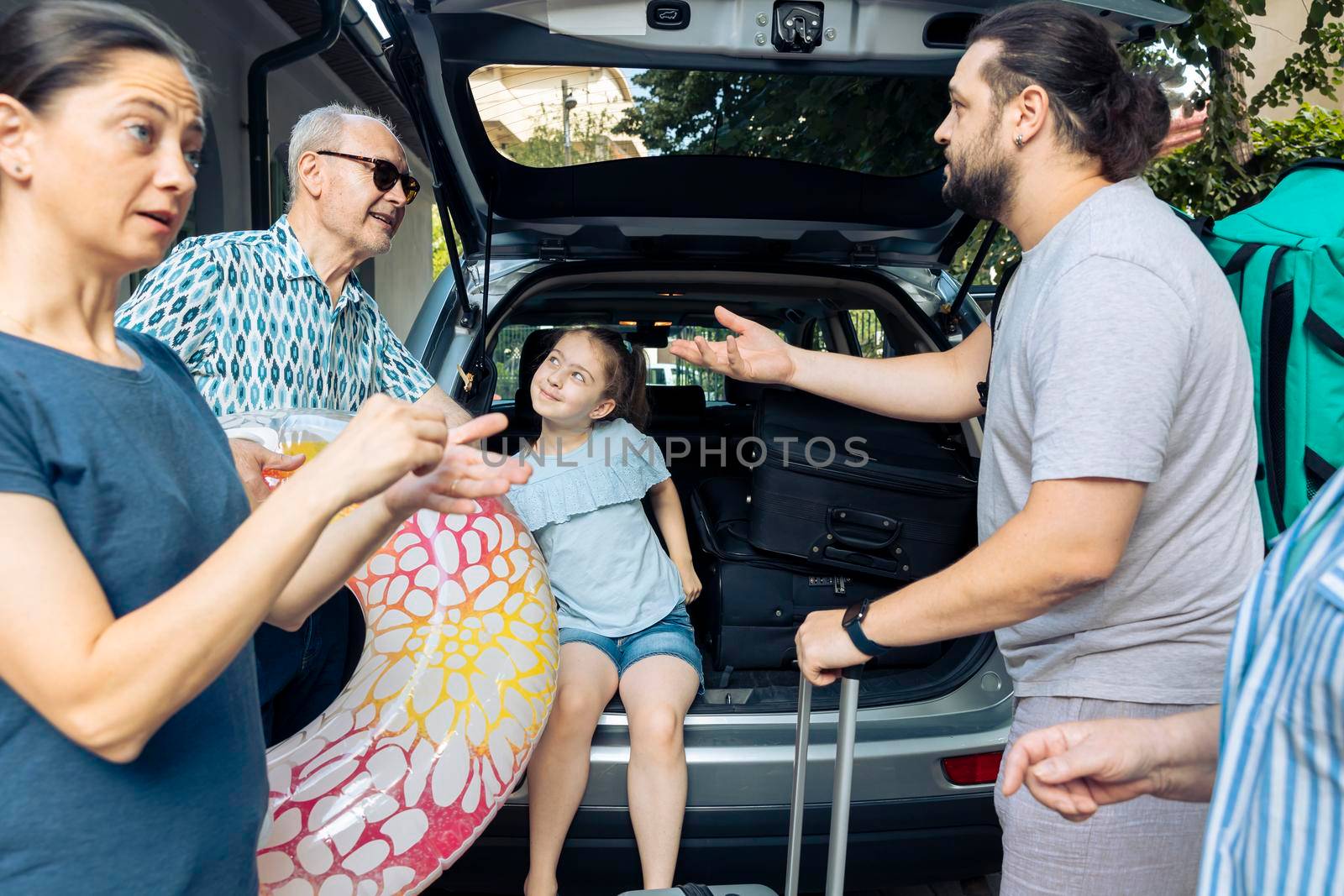 European family travelling on vacation trip, loading baggage and inflatable in car trunk to leave at seaside. Little kid, parents and grandparents going on summer holiday with vehicle.