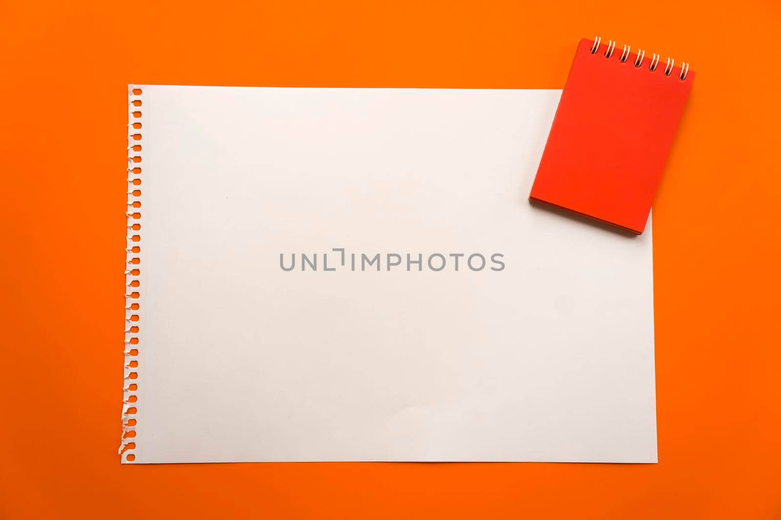 Blank sheet of paper space for design and lettering on a beautiful orange background red notepad sheet. Perforated sheet torn from notepad obliquely lying on the surface. Square sheet of paper copyspace