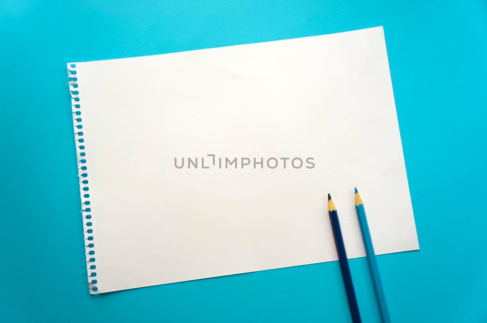 Blank sheet of paper space for design and lettering on a beautiful blue background, blue pencils. A sheet of perforated paper torn from a notepad rests obliquely on the surface. Square sheet copyspace