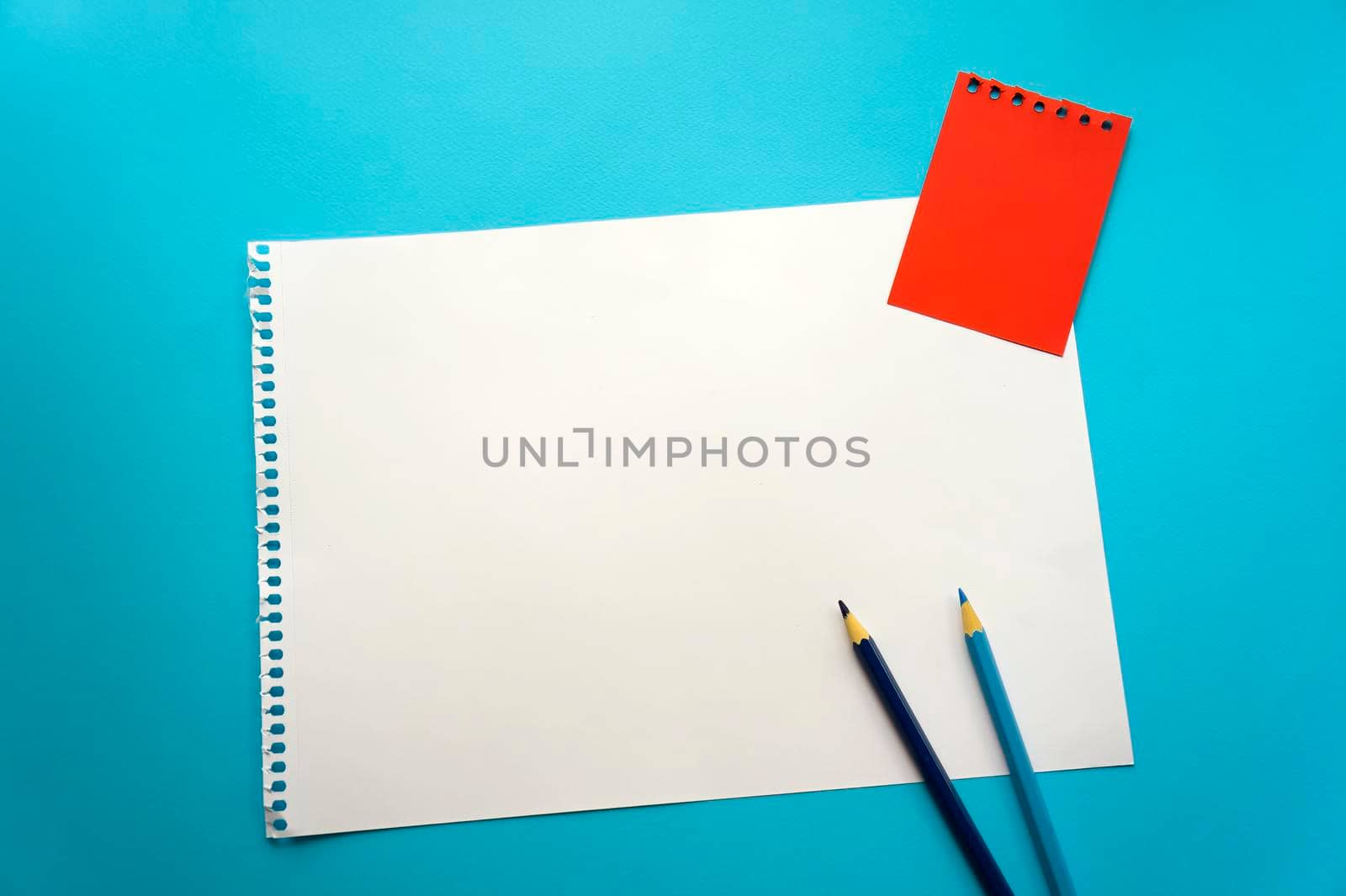 Blank sheet of paper space for design and lettering on a beautiful blue background, blue pencils. A sheet of perforated paper torn from a notepad rests obliquely on the surface. Square sheet copyspace