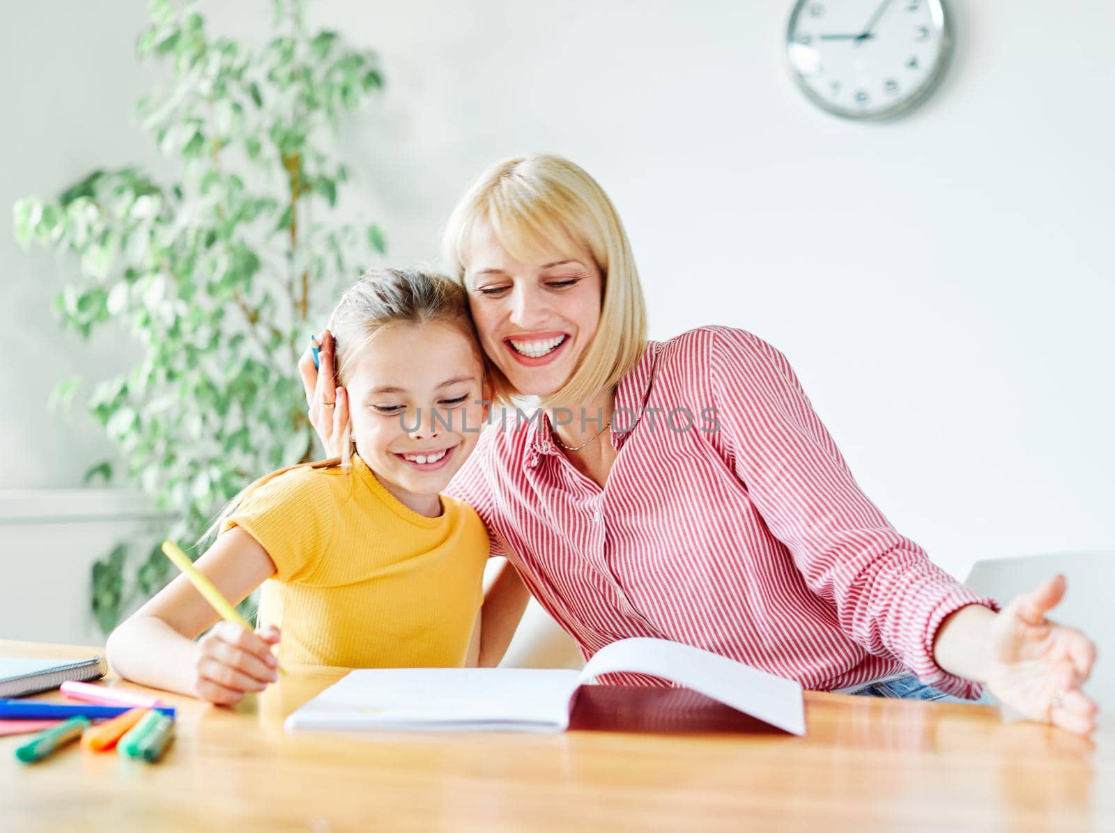 mother or teacher teaching daughter and helping her with homework at home or in classroom