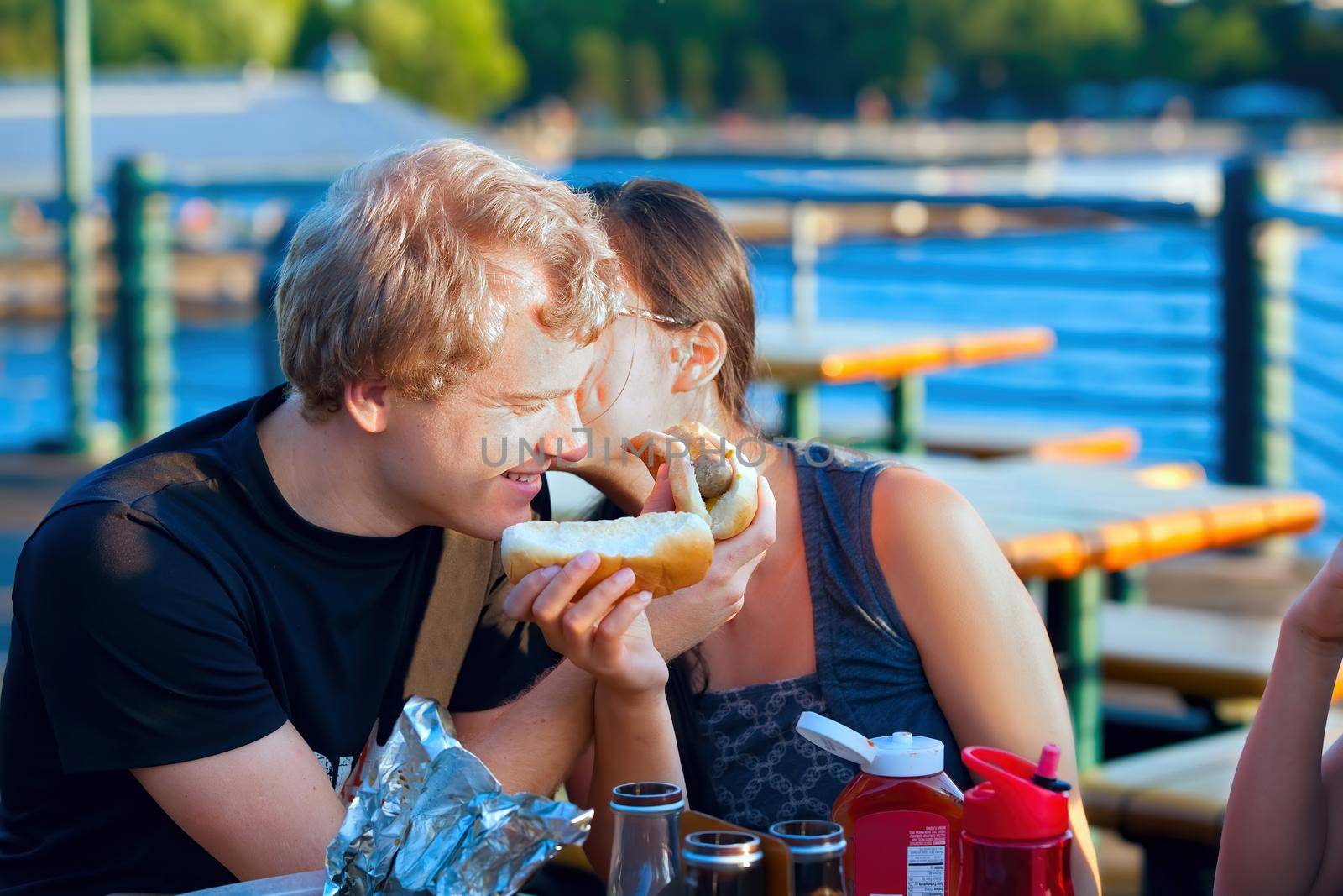 Young couple eating hotdogs  by the lake, having fun