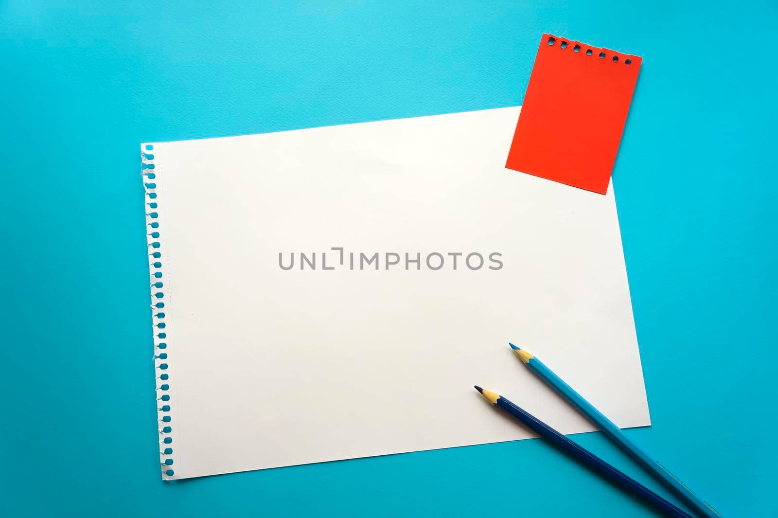 Blank sheet of paper space for design and lettering on a beautiful blue background, blue pencils. A sheet of perforated paper torn from a notepad rests obliquely on the surface. Square sheet copyspace