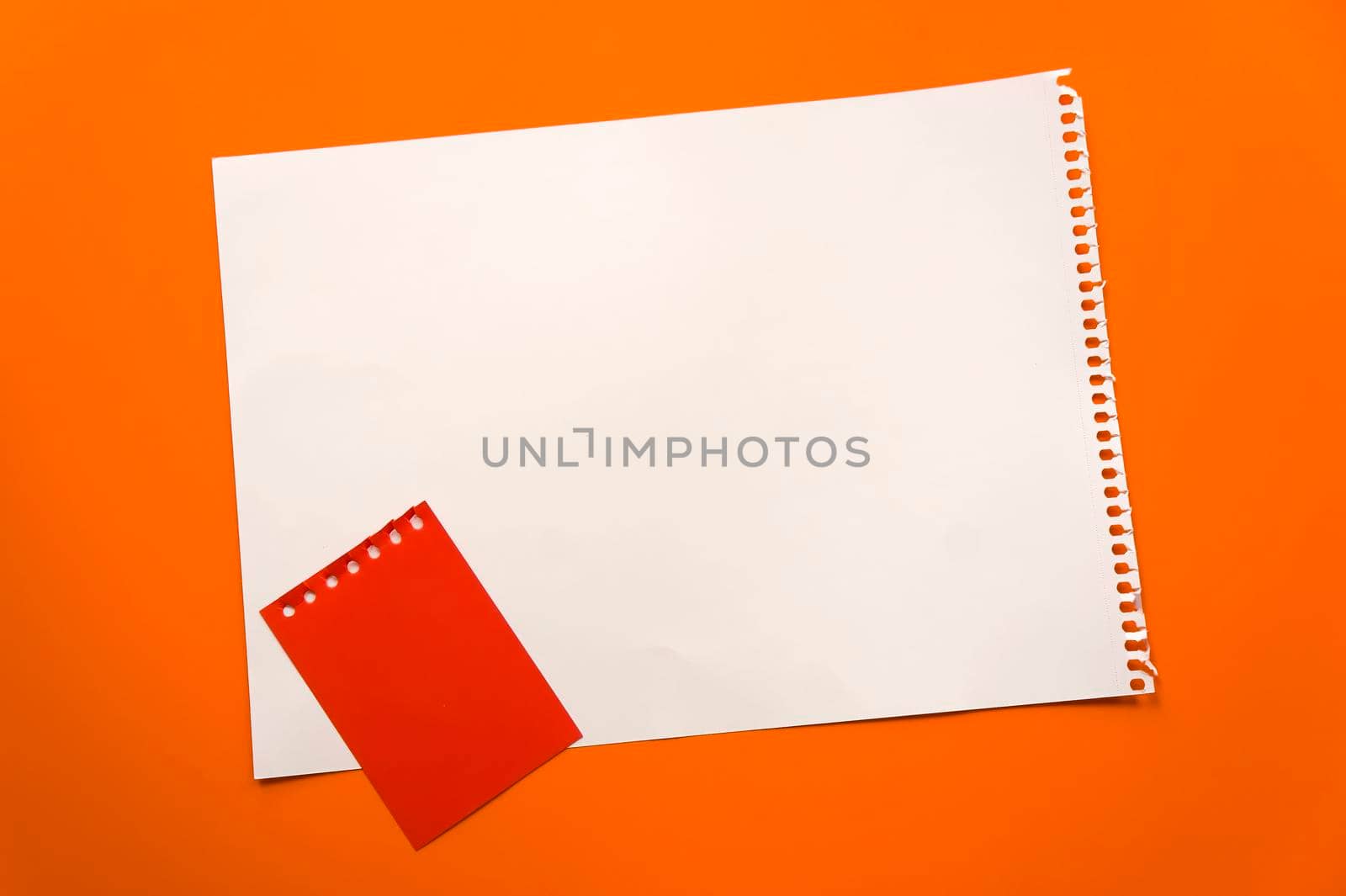 Blank sheet of paper space for design and lettering on a beautiful orange background red notepad sheet. Perforated sheet torn from notepad obliquely lying on the surface. Square sheet of paper copyspace