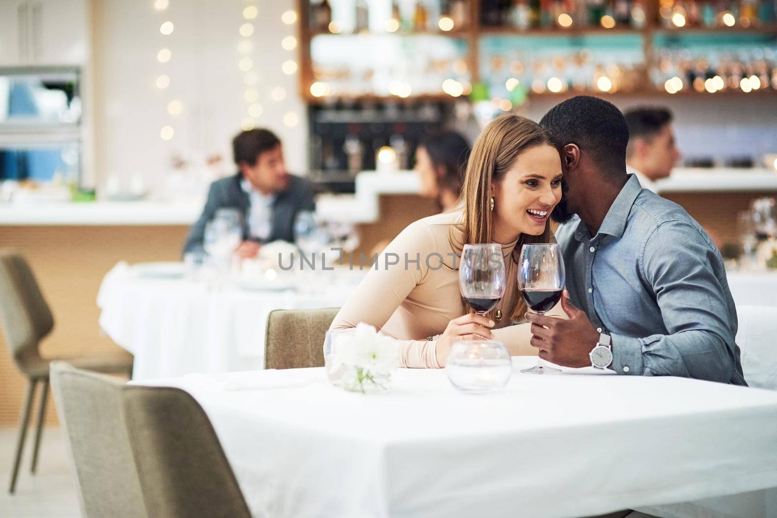 Hes ever so naughty. an affectionate young man whispering into his girlfriends ear while sitting in a restaurant