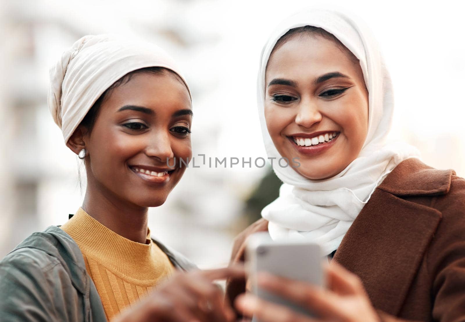 What about this tourist spot here. two attractive young women wearing headscarves and standing together while using a cellphone in the city. by YuriArcurs