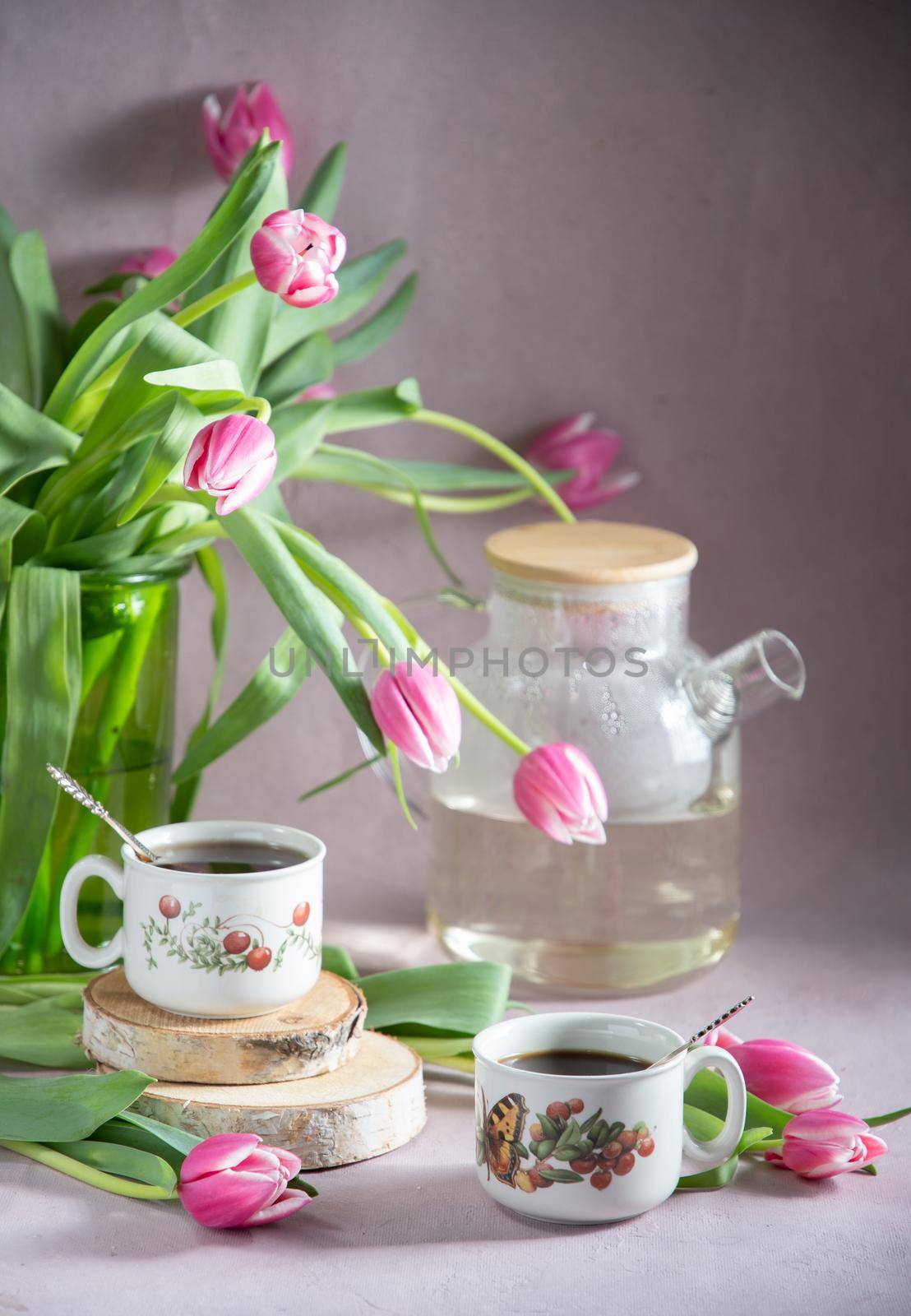 Still life, concept of early spring breakfast with coffee or tea and cupcake on the background of a bouquet of tulips and daffodils