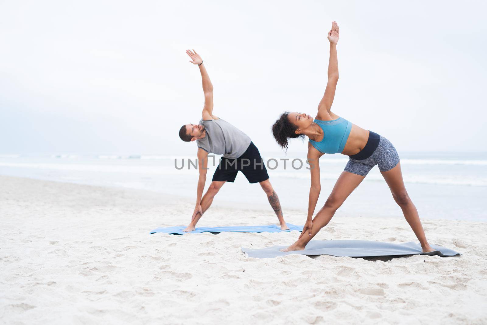 Yoga lies at the core of their wellbeing. a young man and woman practising yoga together at the beach