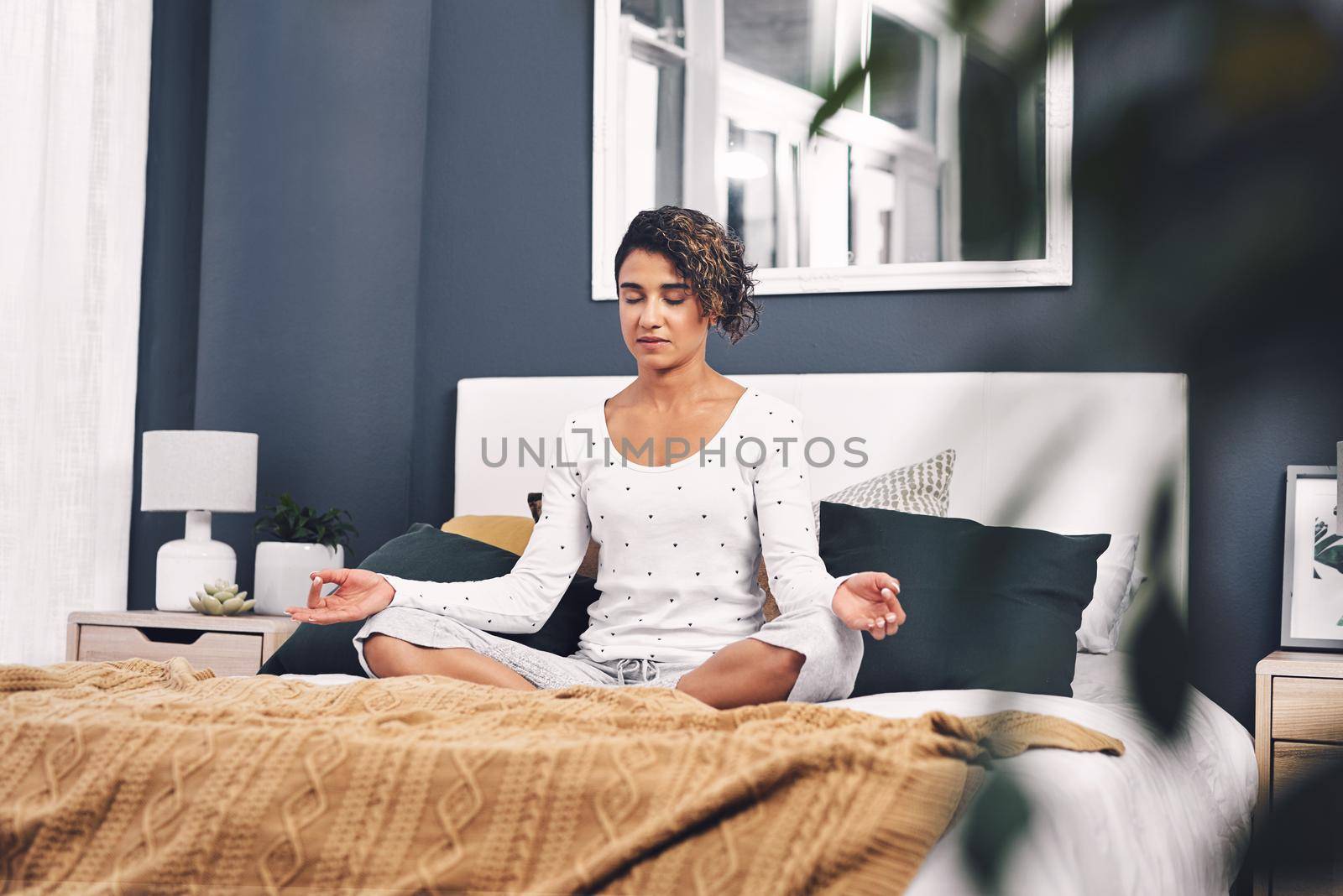Meditation is so important. an attractive young woman sitting and meditating while on her bed at home. by YuriArcurs