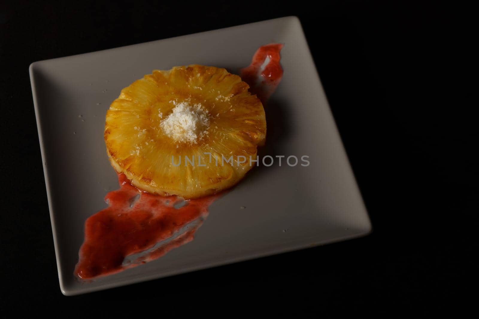 close-up of a grilled natural pineapple with grated coconut on a grey plate on a black background