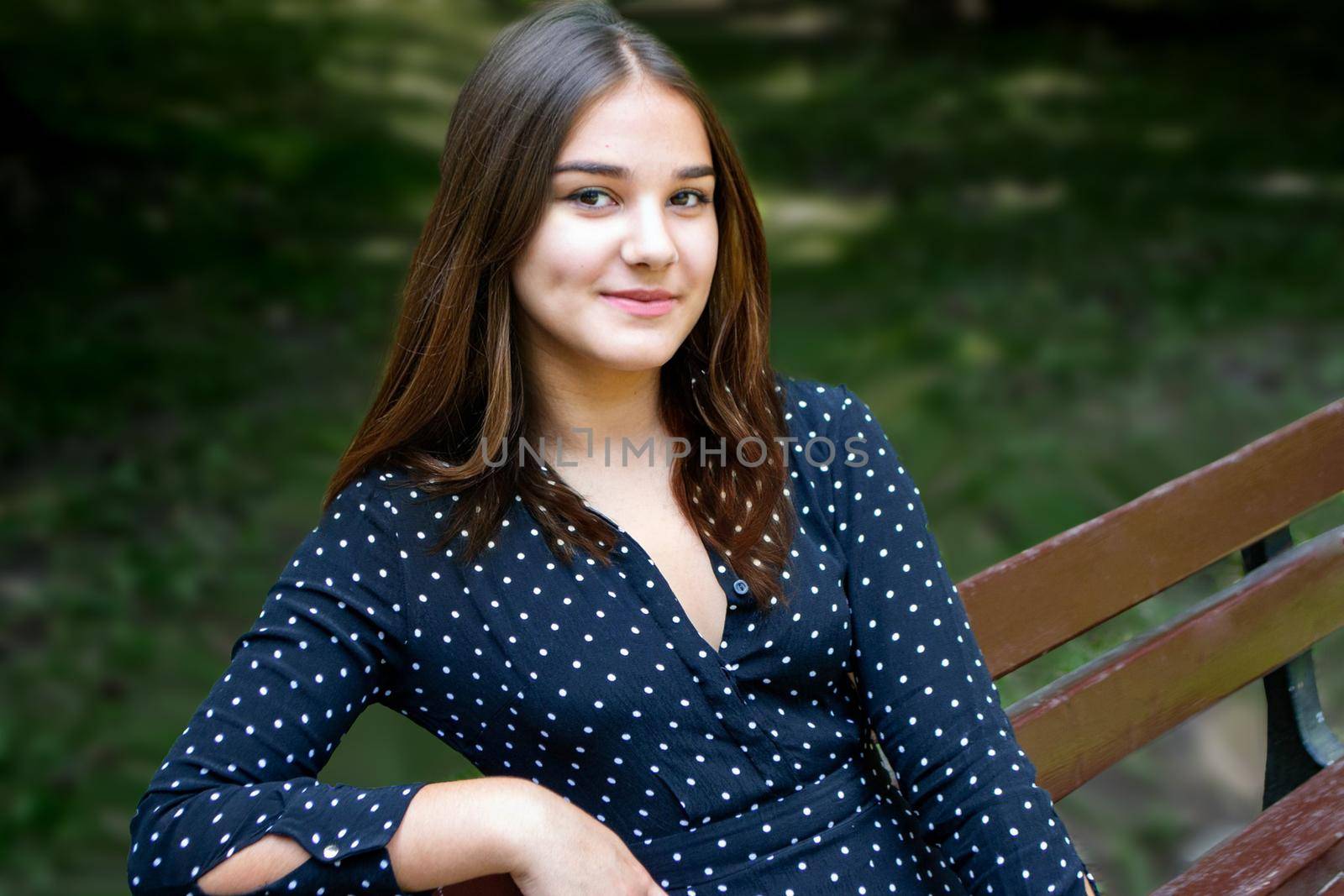 Emotional girl teenager with long hair hairstyle braids in a green shirt sits on a bench in the park. High quality photo