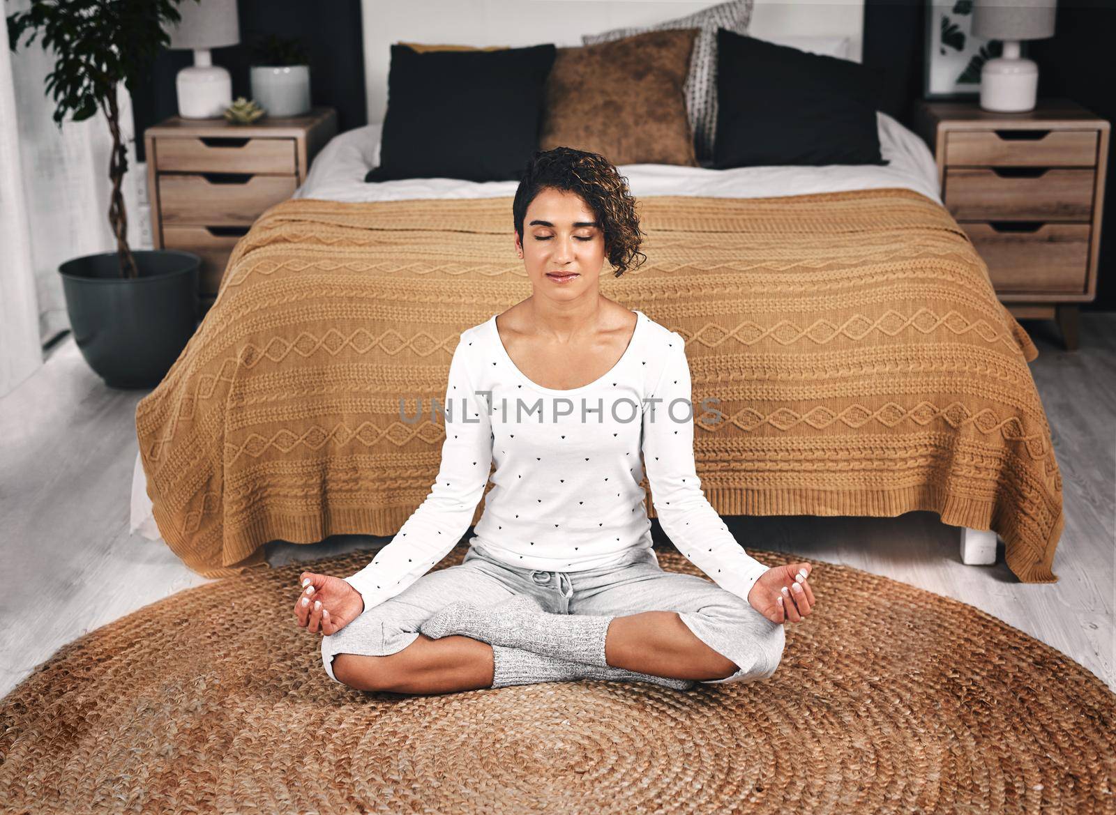 Mental health is just as important as physical health. an attractive young woman sitting and meditating by the foot of her bed in her bedroom. by YuriArcurs