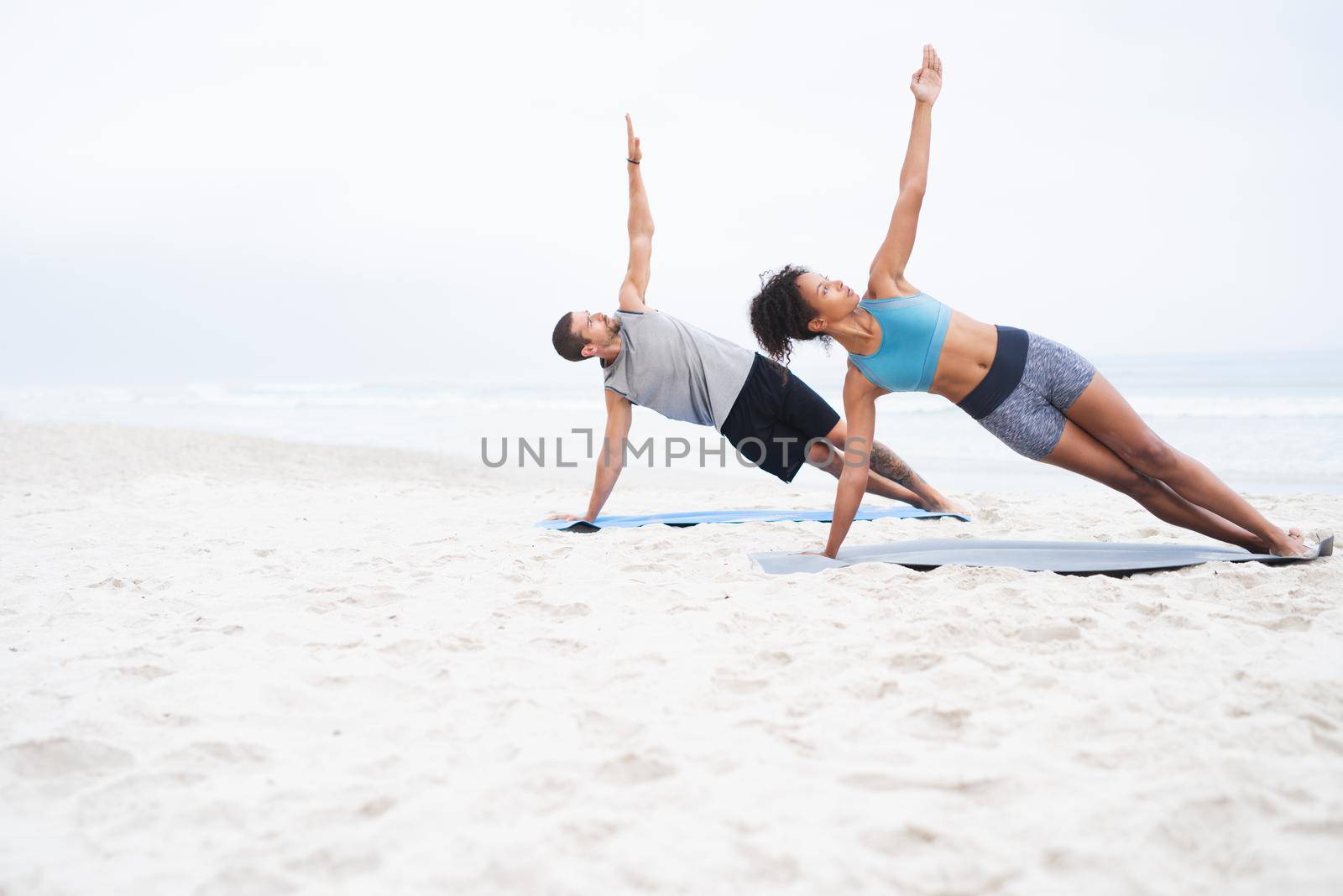 Leading a more active lifestyle together. a young man and woman practising yoga together at the beach. by YuriArcurs