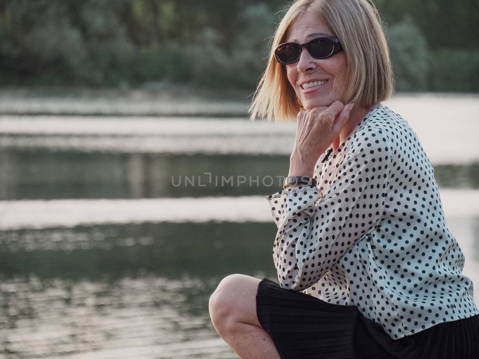 senior lady relaxing in the park wearing sunglasses near the river bank in summer