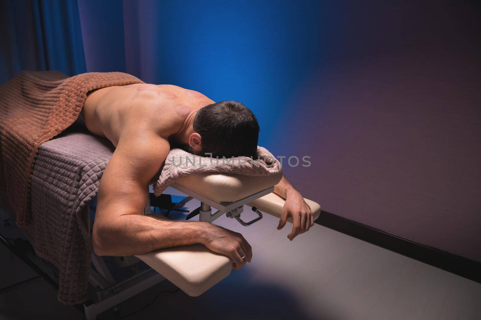 relaxed muscular man lies on massage table in spa center or medical office.