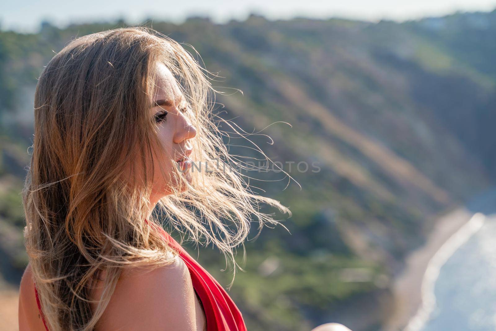 A woman in a red flying dress fluttering in the wind, against the backdrop of the sea