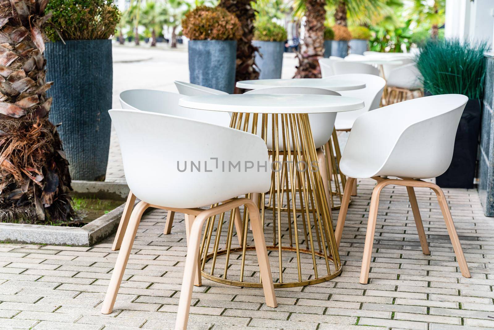 Street cafe with white chairs, green foliage around. Without people, tourism, travel