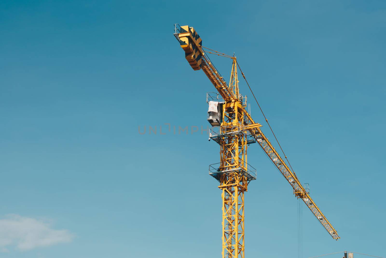Tower Crane lattice boom hook clear blue sky sun background. Construction site work building installation.