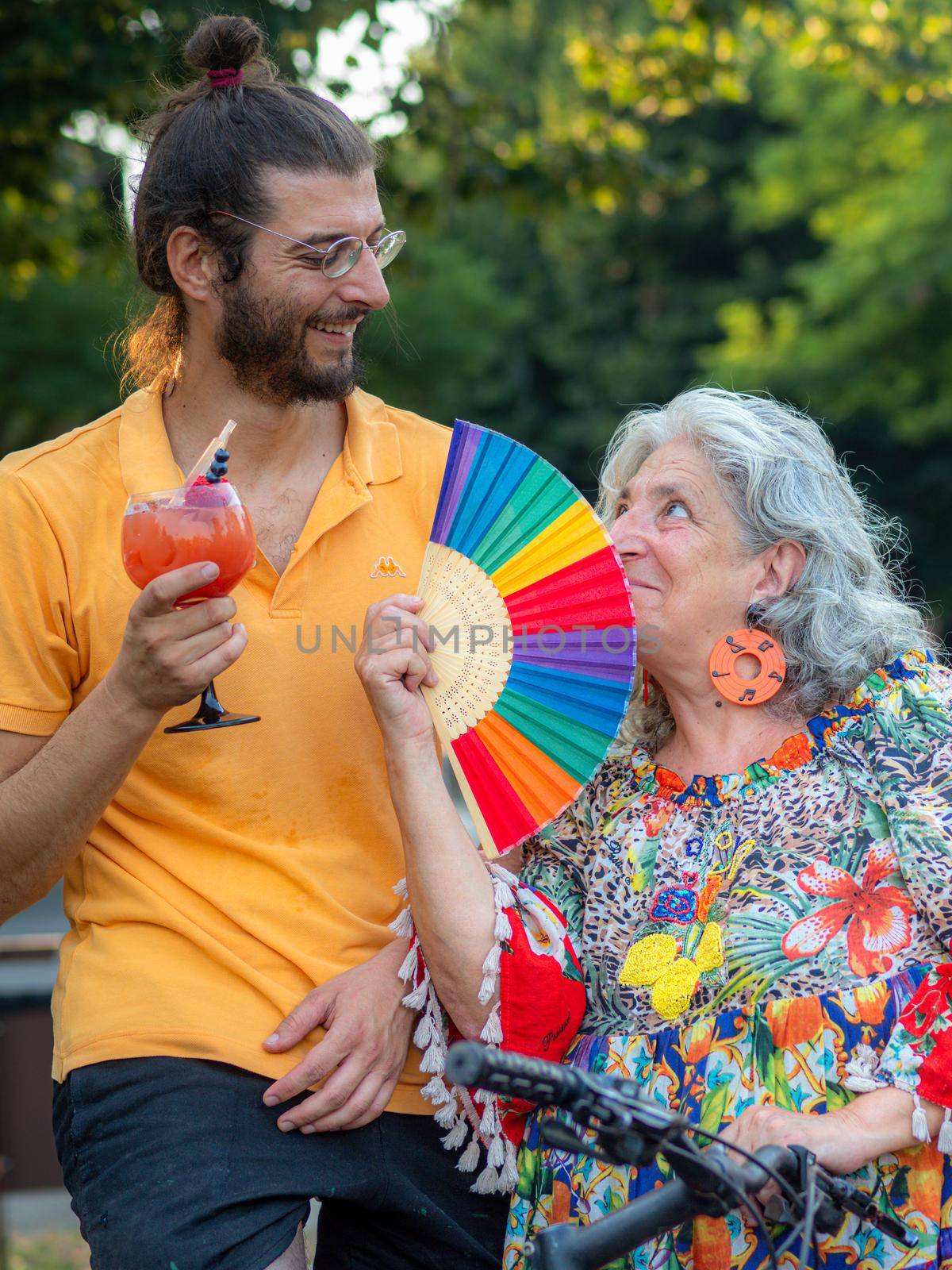 young tall man having a drink hugging mother holding a rainbow colored fan by verbano