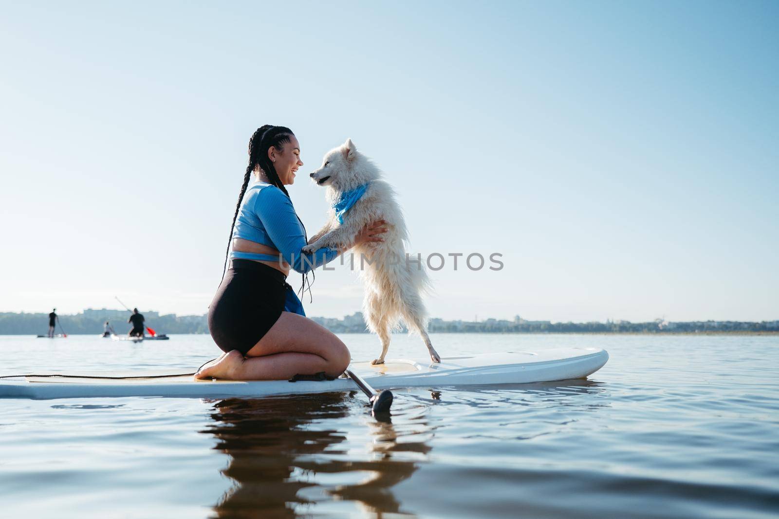 Happy Young Woman with Locs Hugging with Her Dog Japanese Spitz While Sitting on the Sup Board on the Lake by Romvy