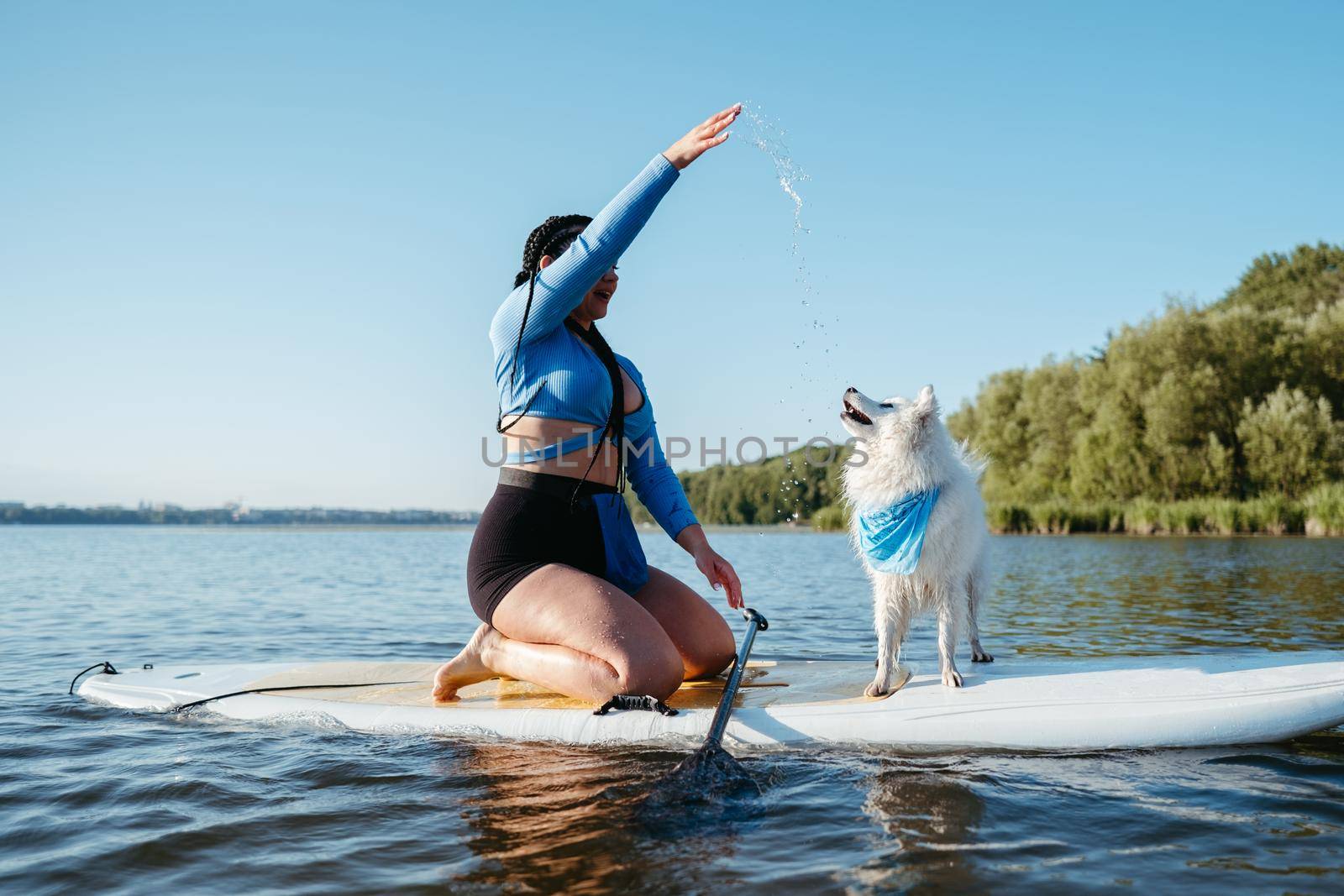 Woman with Locs Playing with Her Pet Japanese Spitz While Sitting on the Sup Board on Lake
