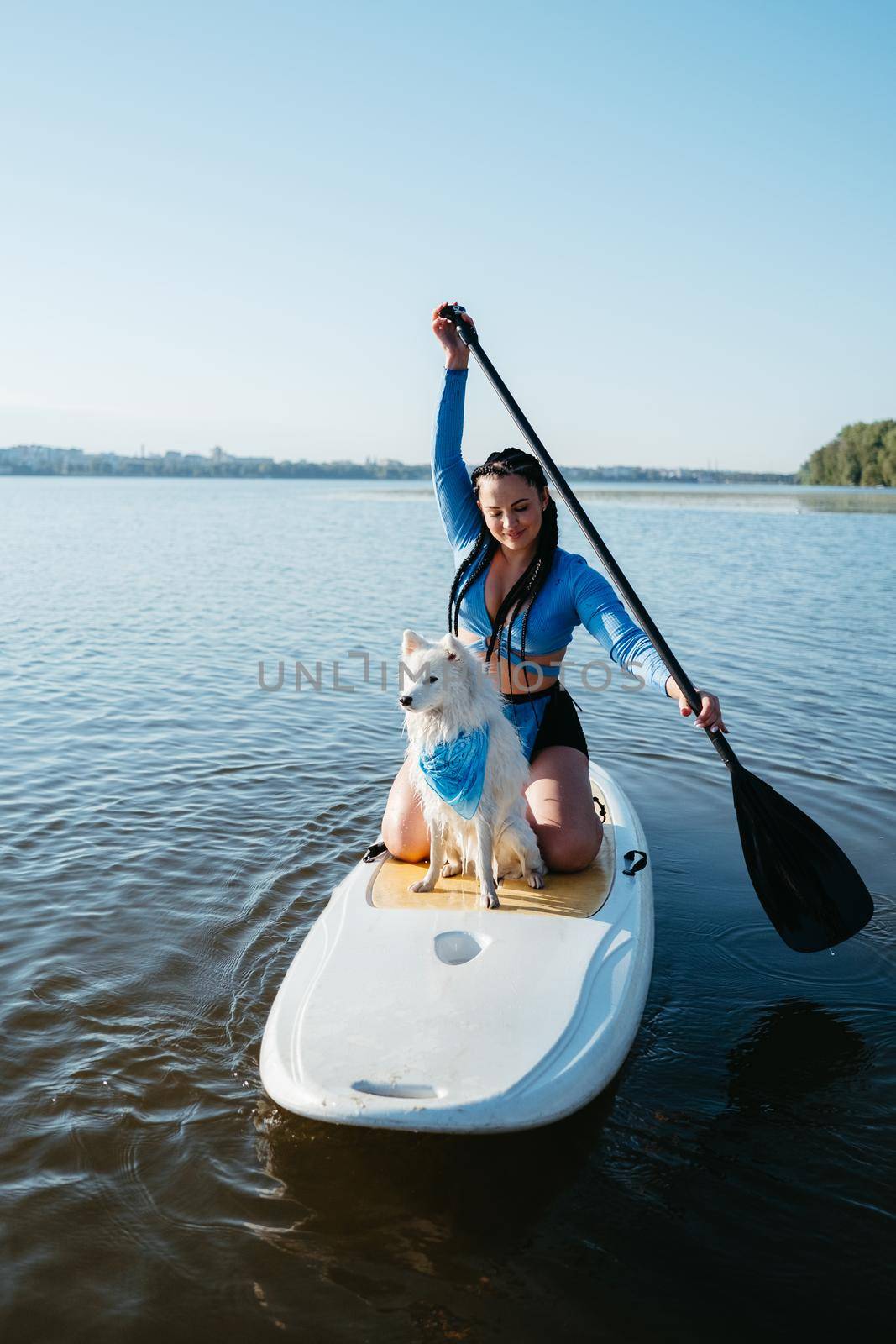 Young Woman with Dreads Paddleboarding with Her Pet on City Lake, Snow-White Japanese Spitz Dog Standing on Sup Board