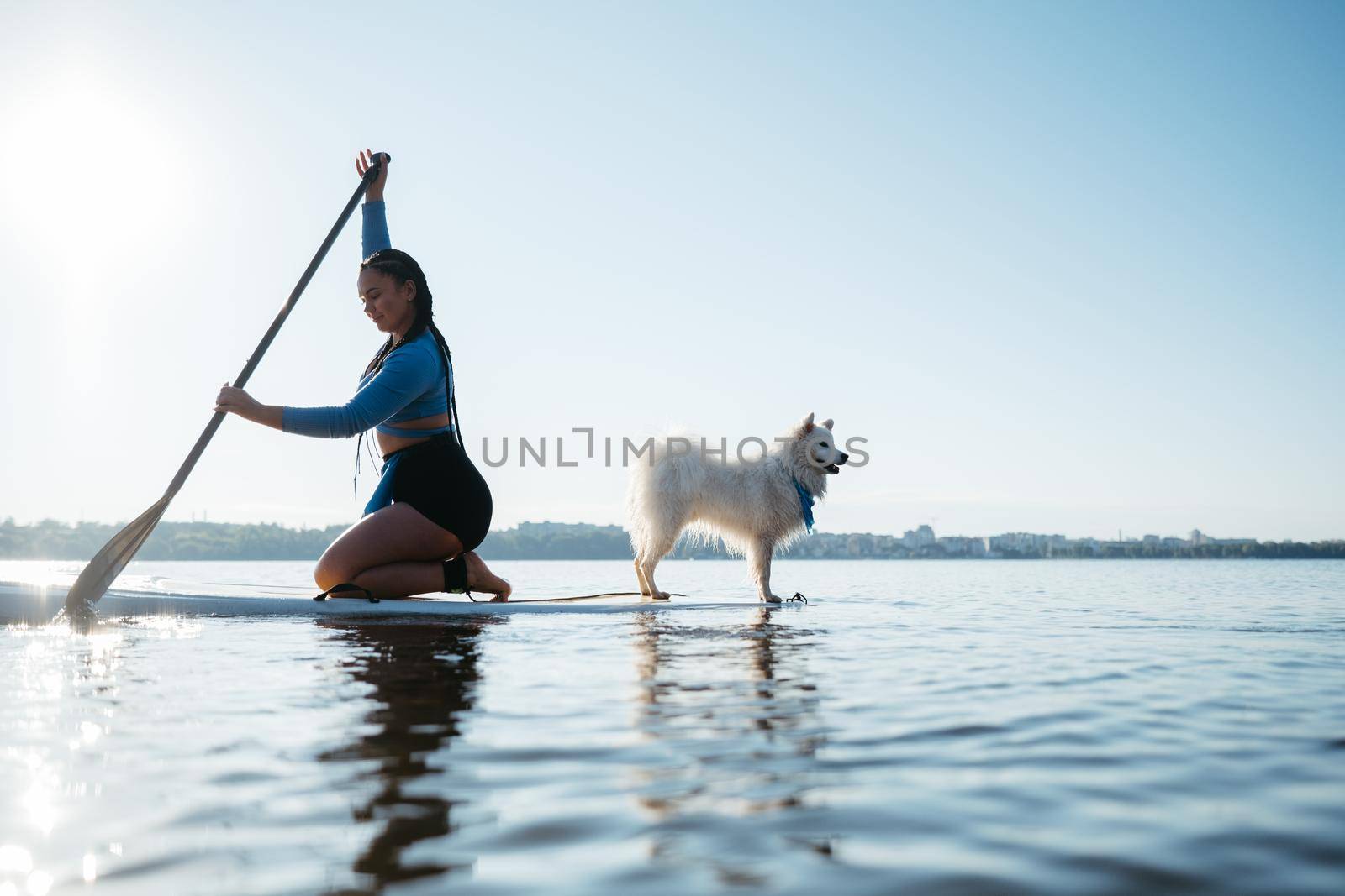 Woman Paddleboarding on the City Lake at Early Morning with Her Dog Japanese Spitz Sitting on the Sup Board by Romvy