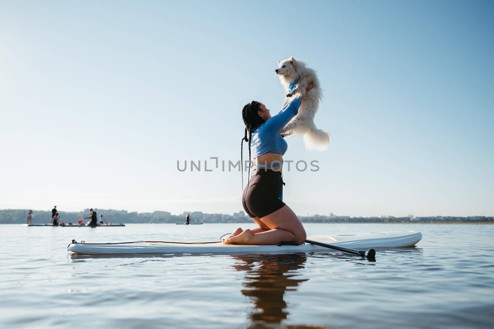 Woman Raising Up Her Dog Japanese Spitz While Sitting on the Sup Board on Lake