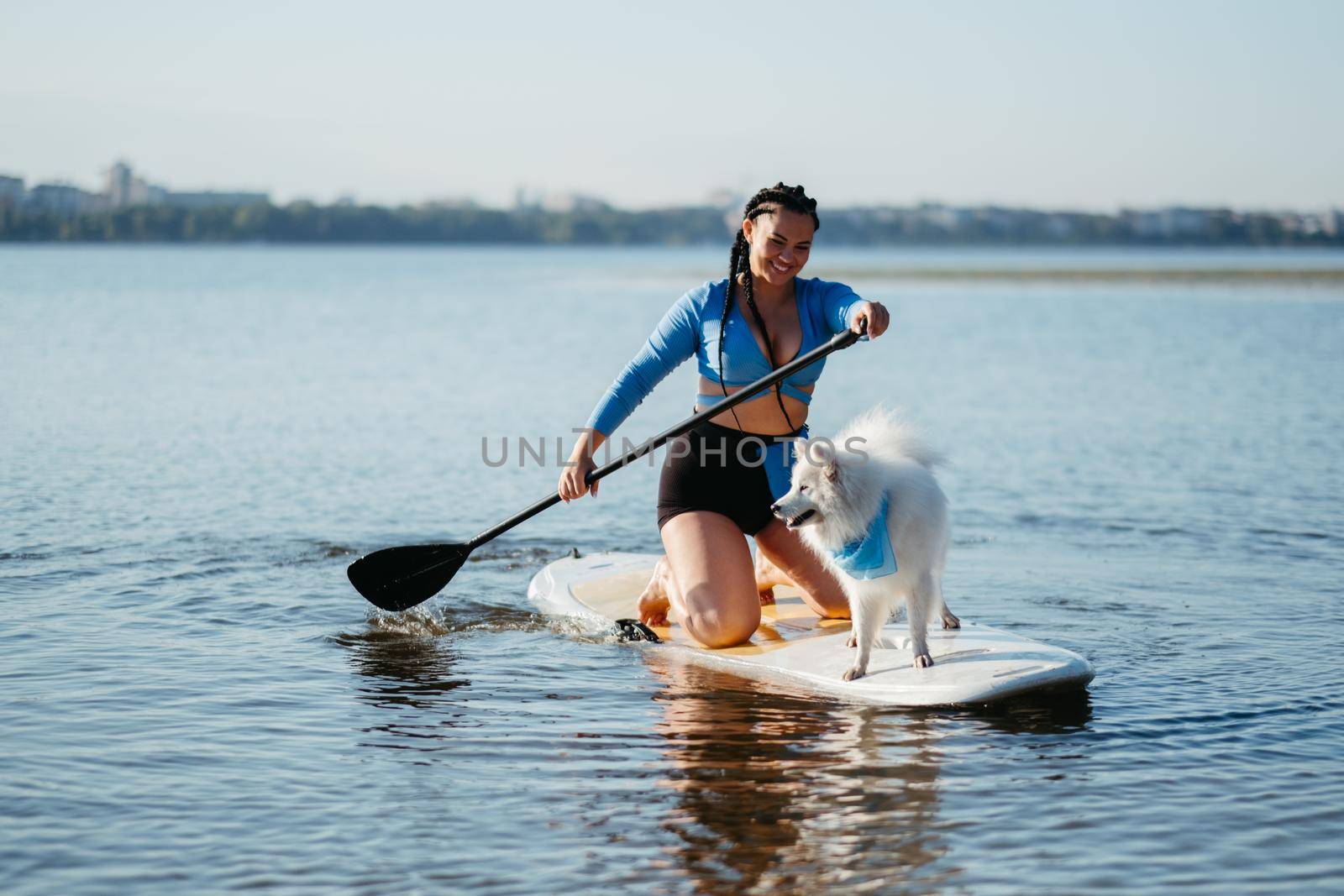 Cheerful Woman with Dreadlocks Paddleboarding with Her Dog Snow-White Japanese Spitz on Sup Board on City Lake