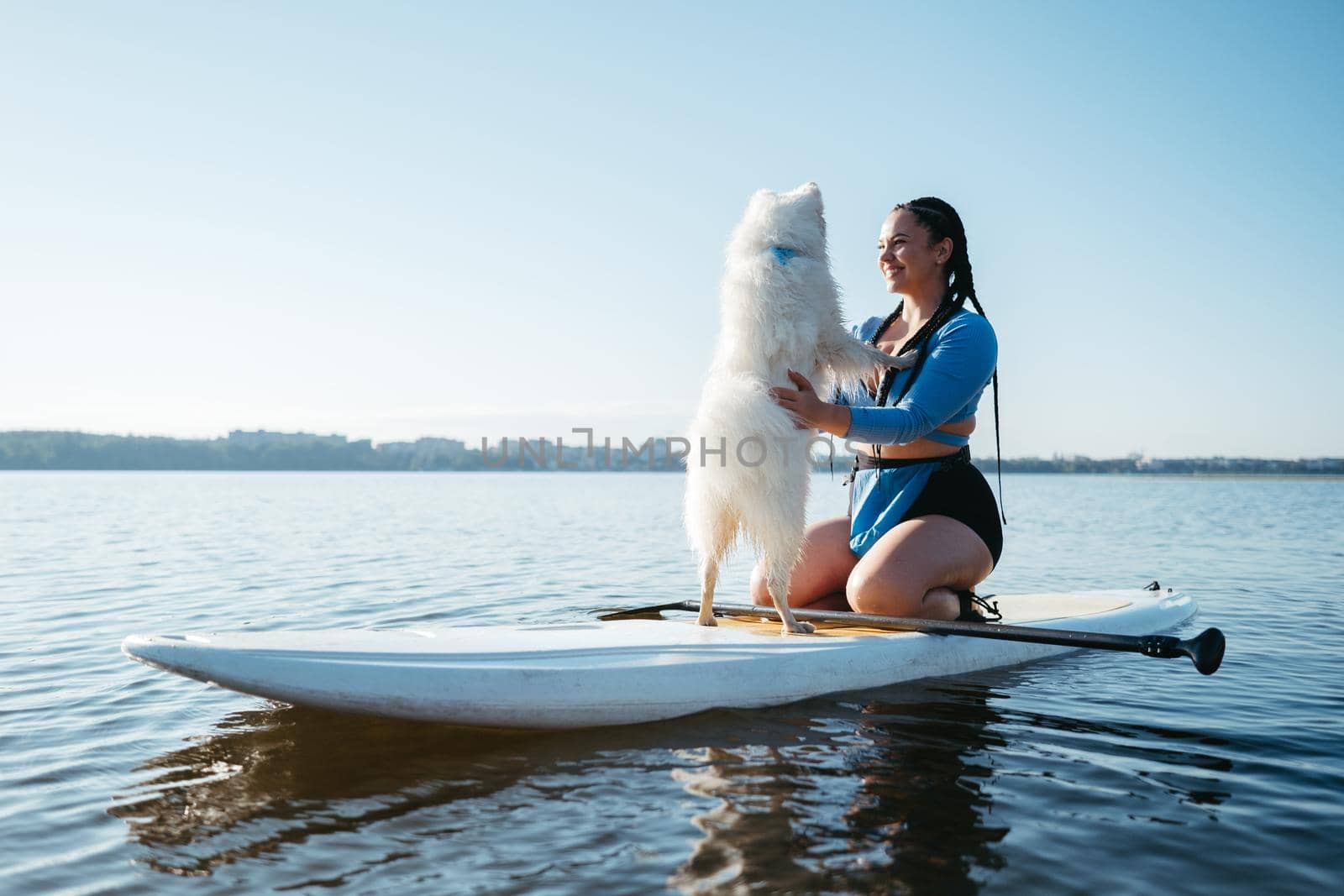 Happy Young Woman Hugging with Her Dog Japanese Spitz While Sitting on the Sup Board on the City Lake at Sunrise by Romvy