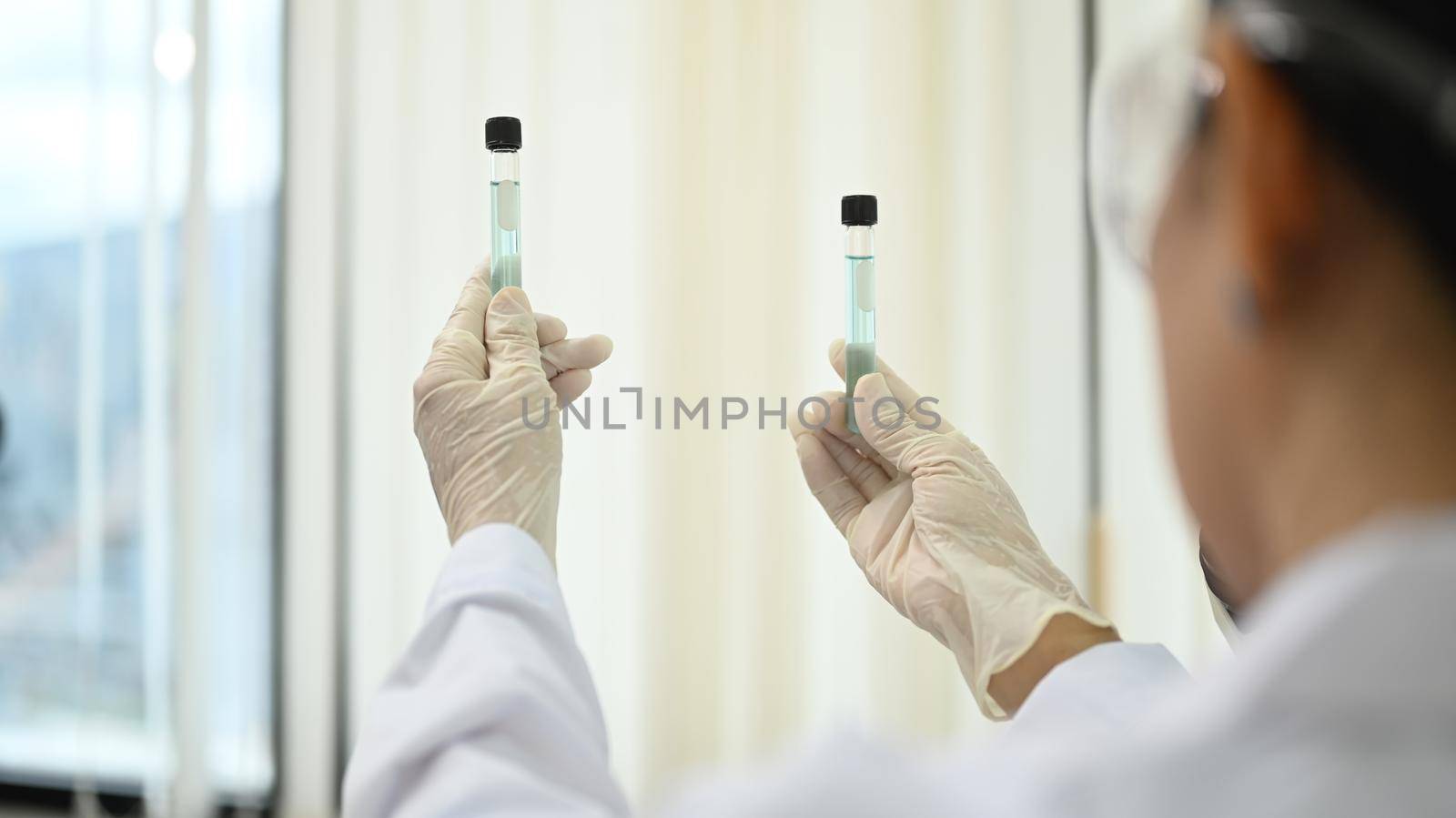 Over shoulder view of professional chemist holding test tube while researching and examining in laboratory by prathanchorruangsak