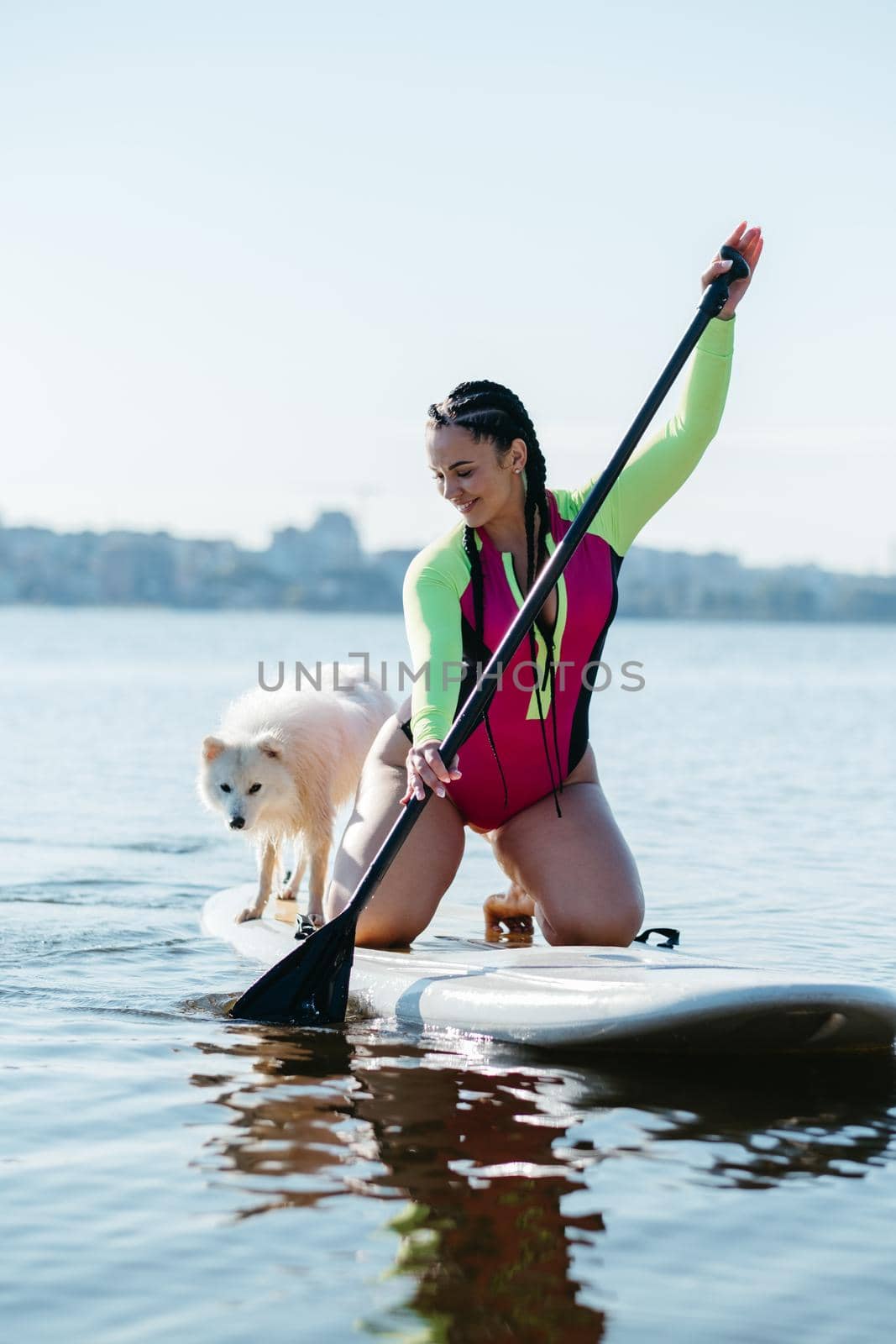 Happy Cheerful Woman Paddleboarding on the City Lake at Early Morning with Her Dog Japanese Spitz Sitting on the Sup Board by Romvy