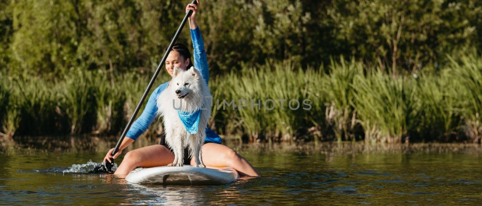Young Woman Paddleboarding with Her Pet on the Lake, Snow-White Dog Breed Japanese Spitz Standing on Sup Board