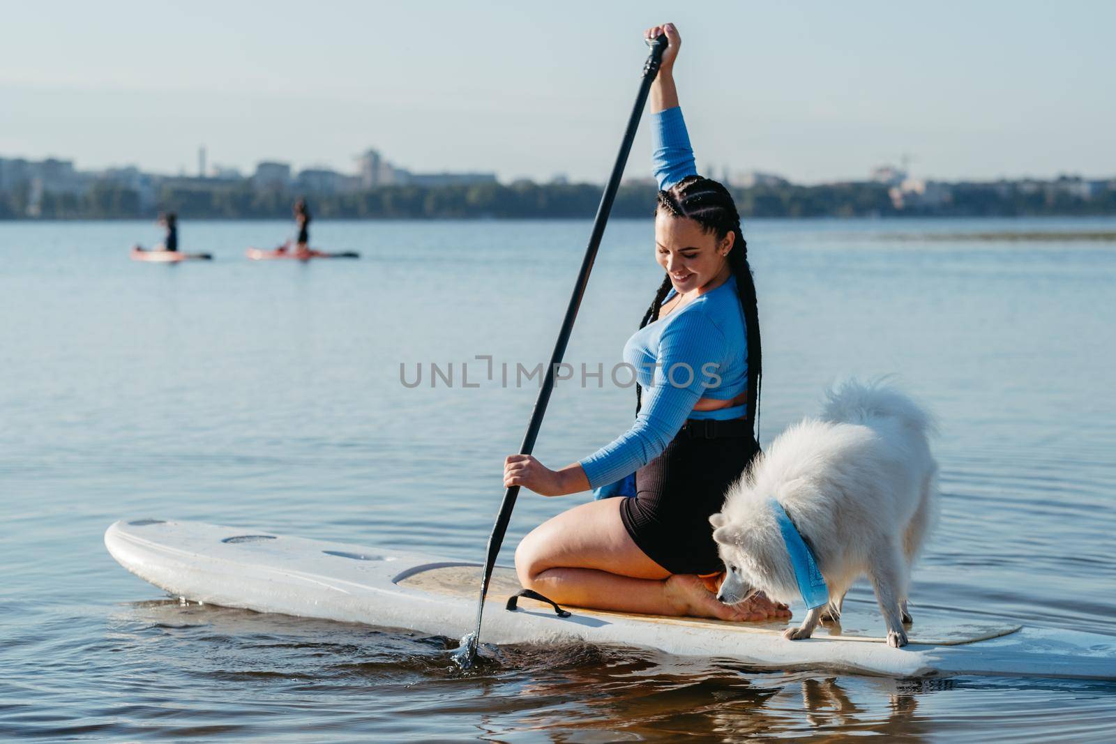 Woman with Dreadlocks Paddleboarding with Her Dog Snow-White Japanese Spitz on Sup Board on City Lake