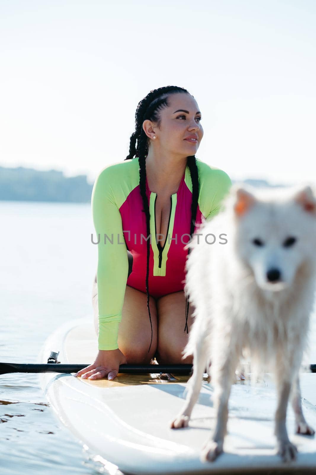 Portrait of Young Woman with Dreadlocks in Swimwear Sitting on the Sup Board with Her Dog Japanese Spitz by Romvy