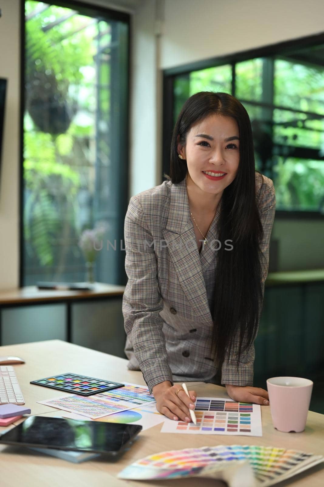 Beautiful asian woman standing at her creative office and smiling to camera.