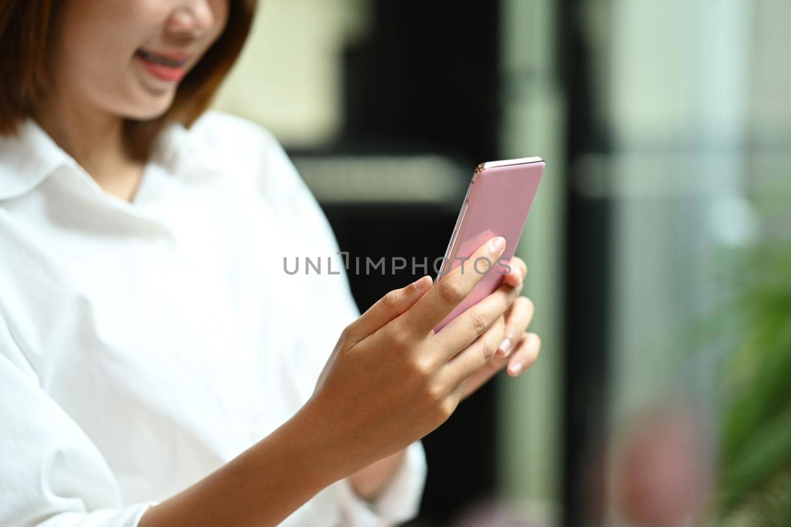 Smiling young asian woman sitting in office and using mobile phone.