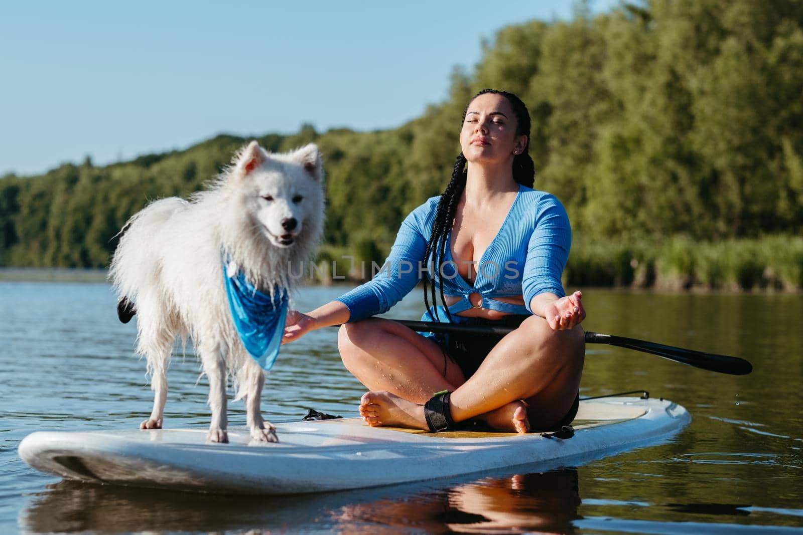 Young Woman Meditating on the City Lake While Sitting on Sup Board with Her Dog Japanese Spitz